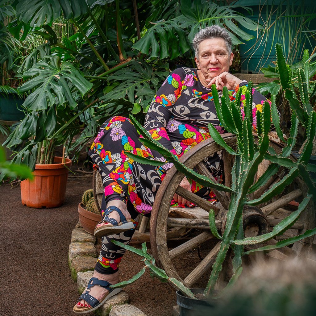 A mature woman wearing a colorful MAGICAT black midi dress and yoga leggings.