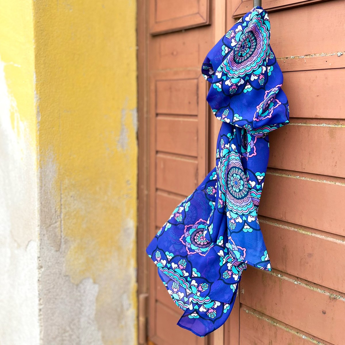 A colorful scarf hanging on a door handle outdoors. Design: FOREVERMORE purple.