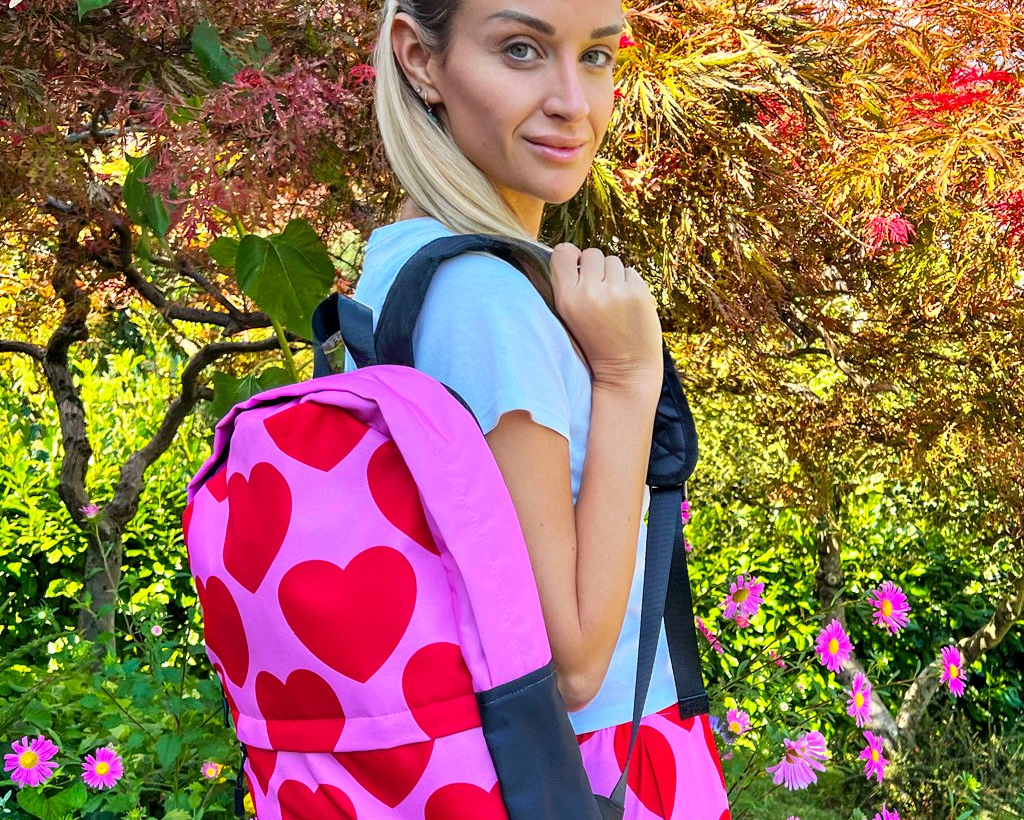 Woman and a colorful backpack with red hearts on pink.